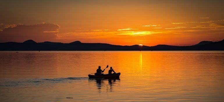 Two people on a boat sailing in clear water during sunset