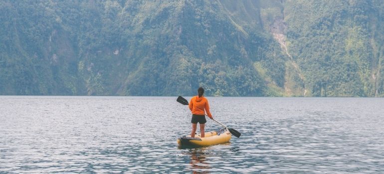 A woman stands on a kayak and thinks about packing and moving water sports equipment in San Leandro.