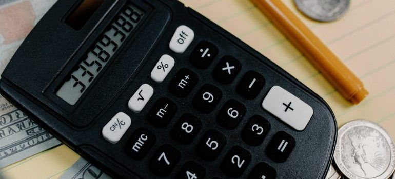 A calculator is sitting on top of a table next to a pen and coins.