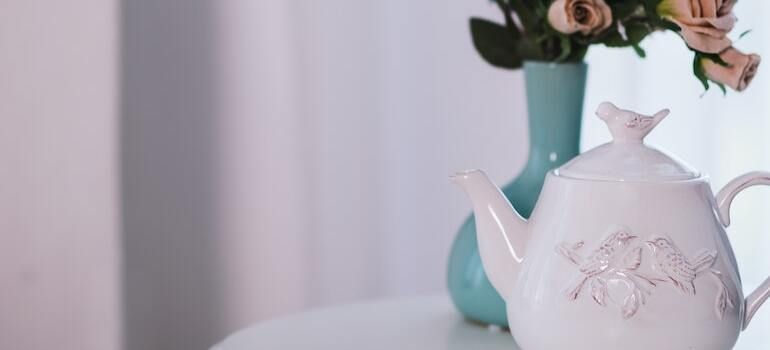 A white teapot is sitting on a table next to a vase of flowers.