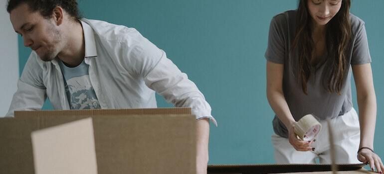 A man and a woman are packing boxes in a room.