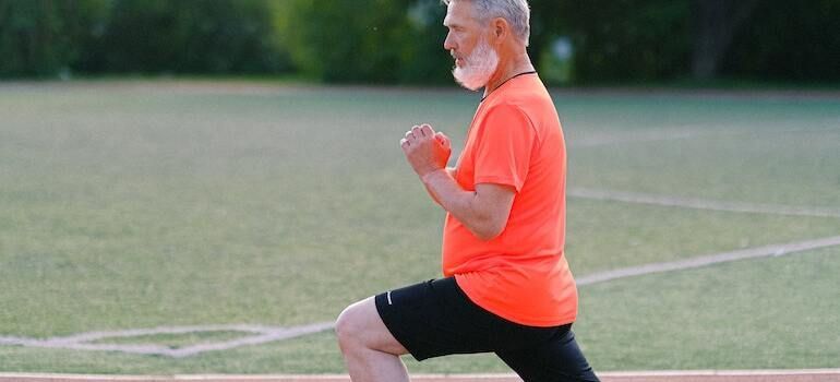 An elderly man is stretching his legs on a soccer field.