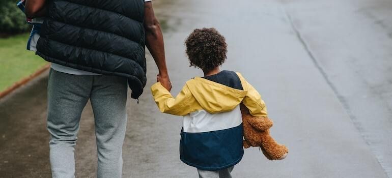 A man and a child are walking down a street holding hands.