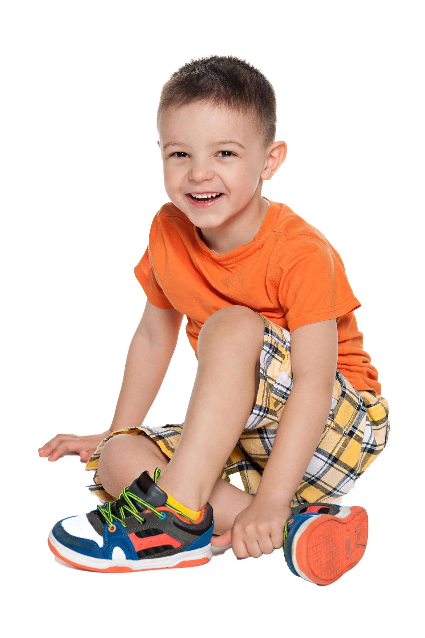 Smiling child in orange shirt and plaid shorts sits on the floor, next to a shoe. Smiling child in orange shirt and plaid shorts sits on the floor, next to a shoe.