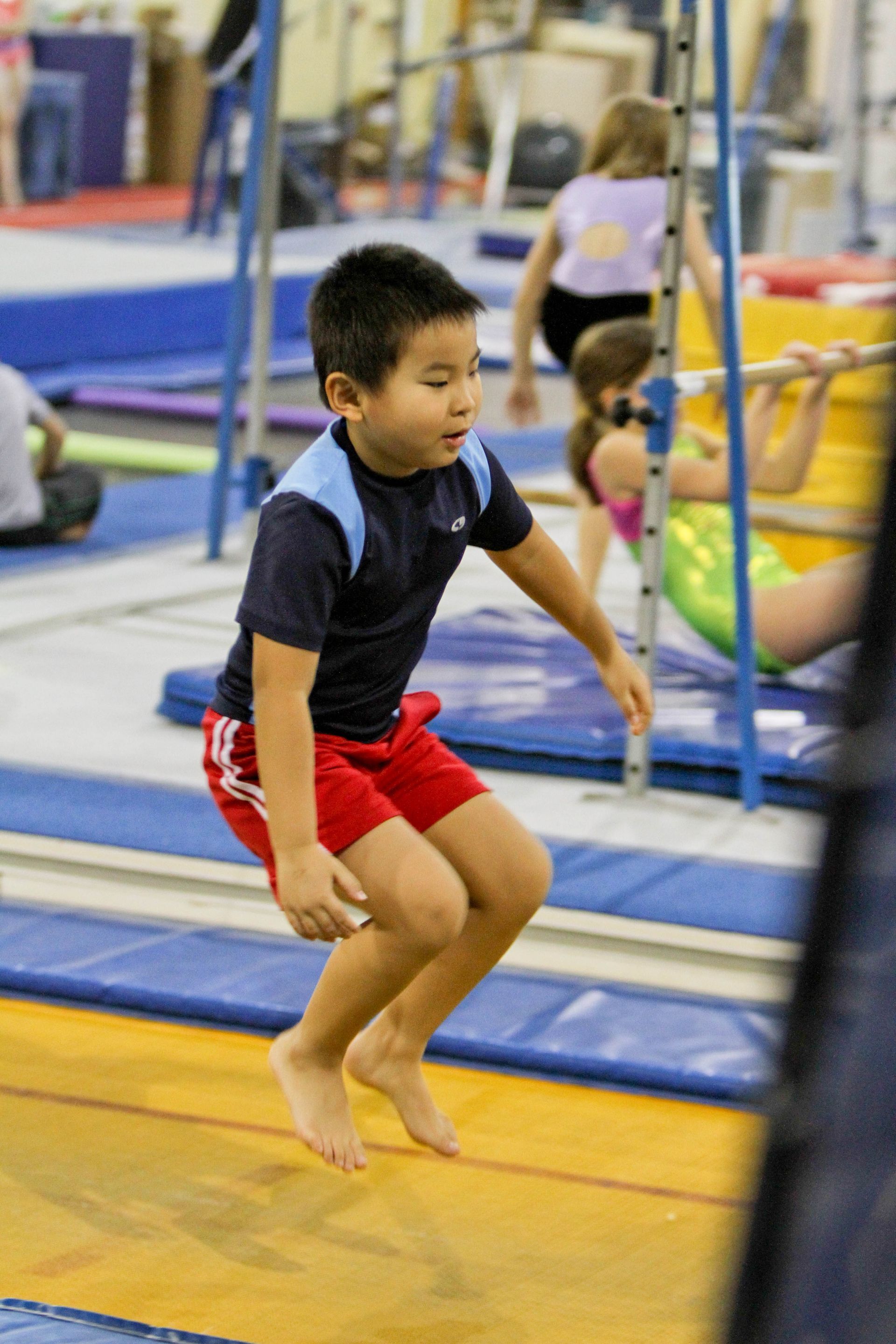 A young boy is jumping on a balance beam in a gym.