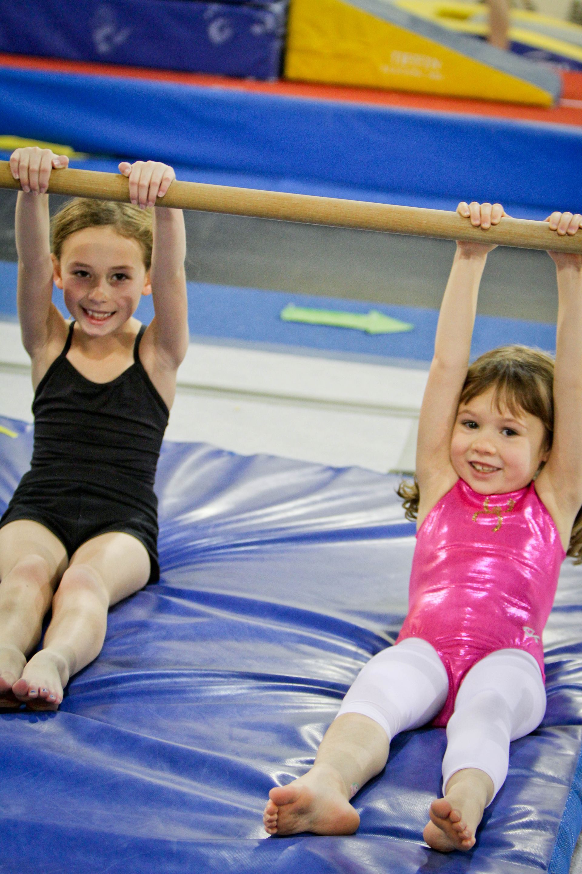 Two little girls are hanging from a bar in a gym