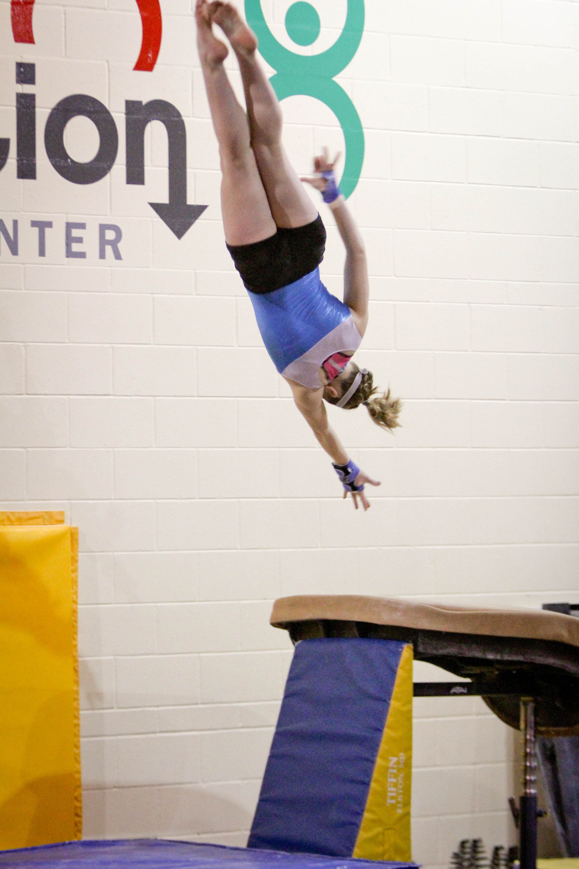 A female gymnast is doing a handstand on a balance beam.