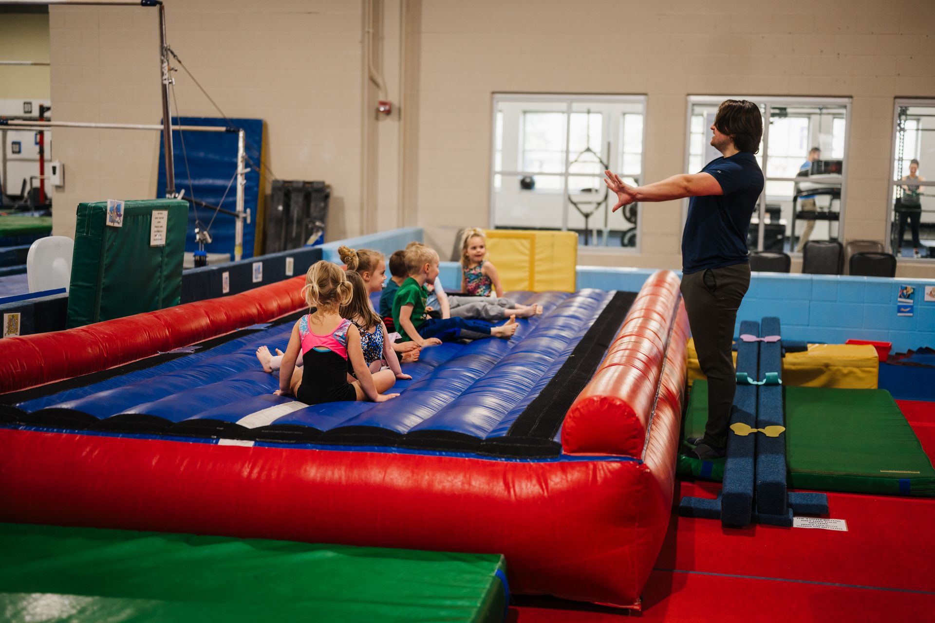 A group of young girls are sitting on a trampoline in a gym.