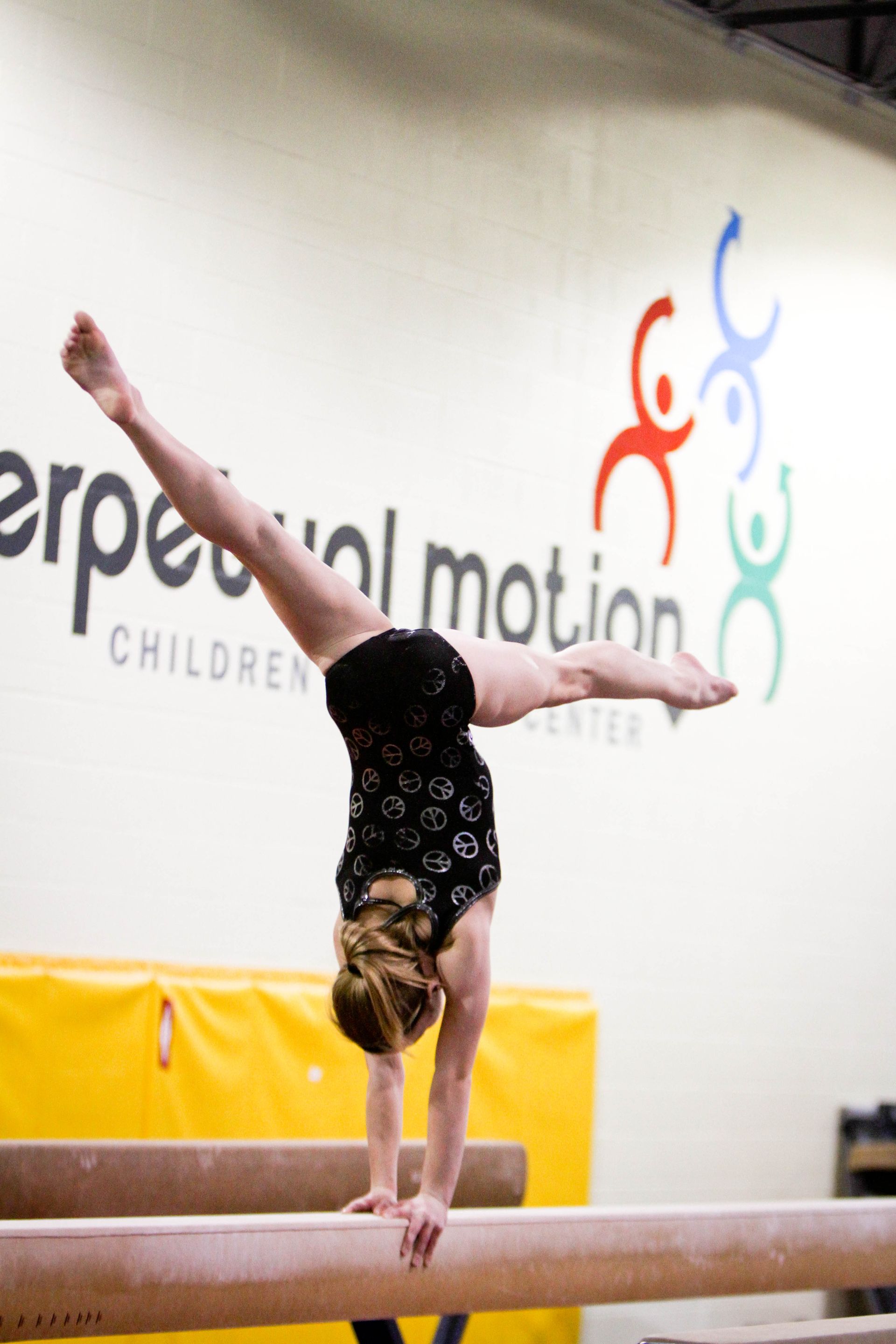 A girl is doing a handstand on a balance beam in front of a sign that says erpecial motion children 's center