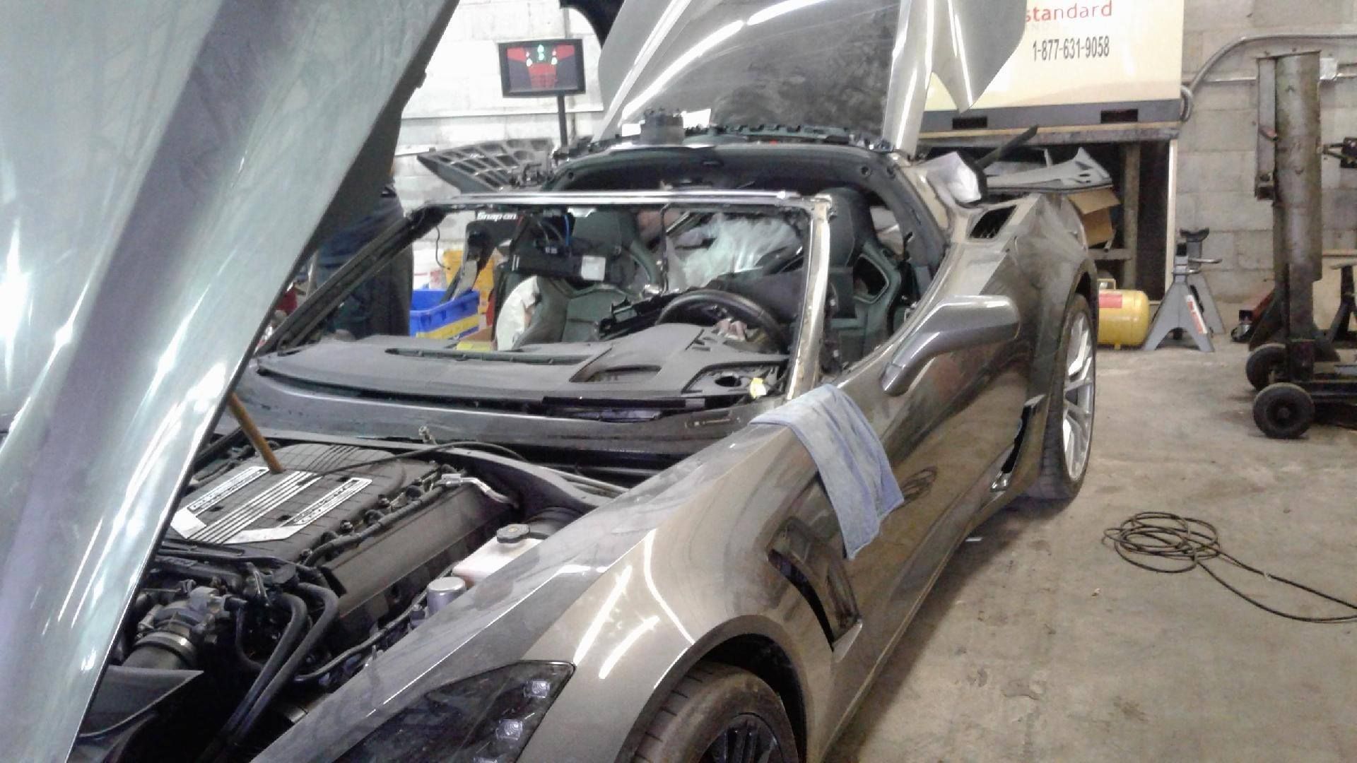 Gray Corvette convertible with hood and doors open in a garage, being worked on.