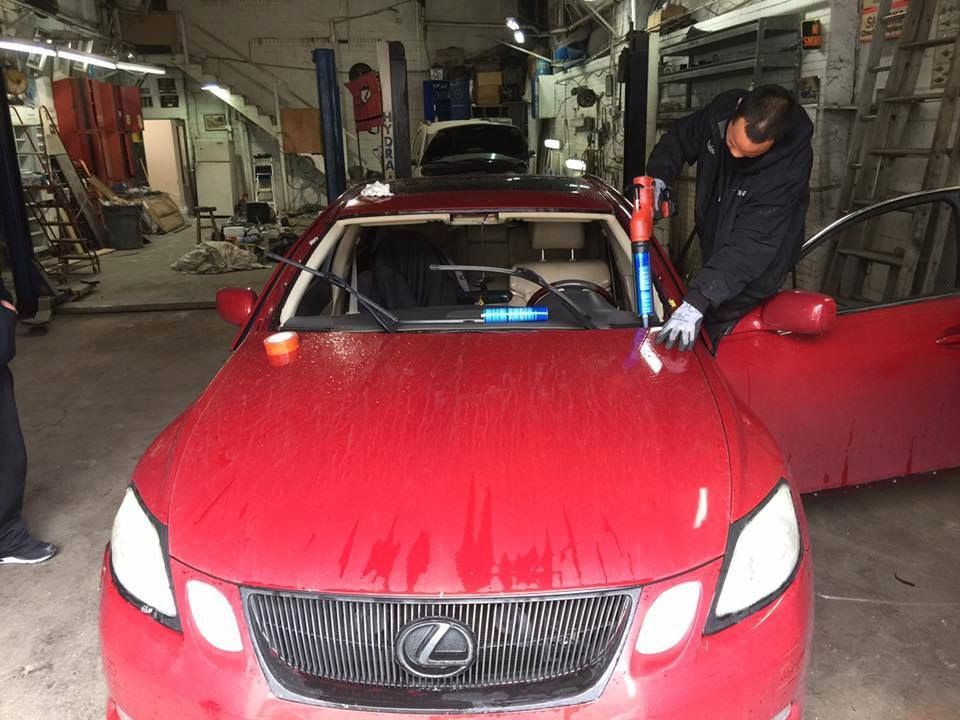 Red car in a garage; a person is working on the windshield with tools.