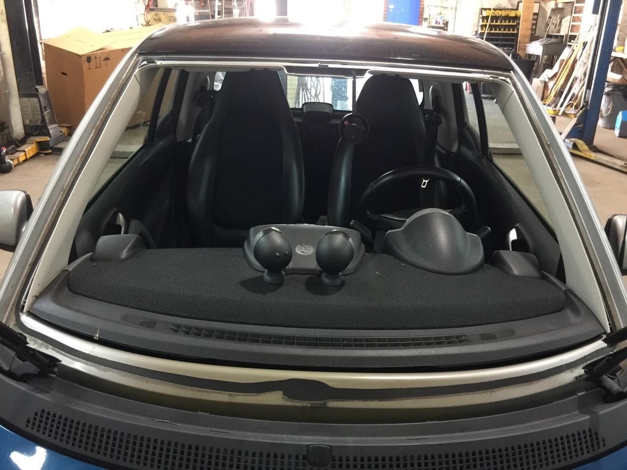 Interior view of a small blue Smart car, showing black seats, steering wheel, and windshield.