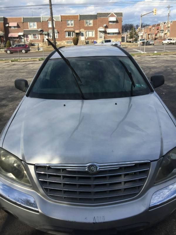Silver Chrysler PT Cruiser car parked in front of brick buildings on a sunny day. Windshield wipers raised.