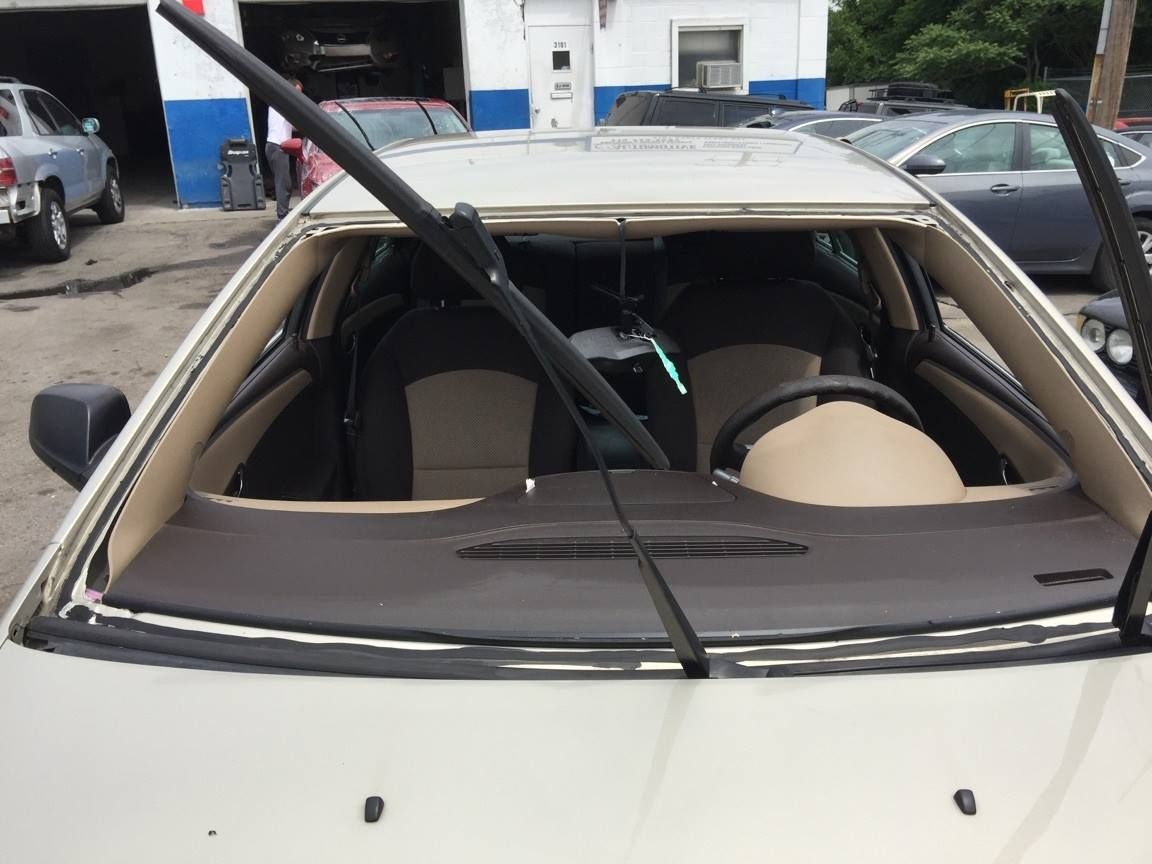 Car with a cracked windshield parked outside a repair shop; wipers up.