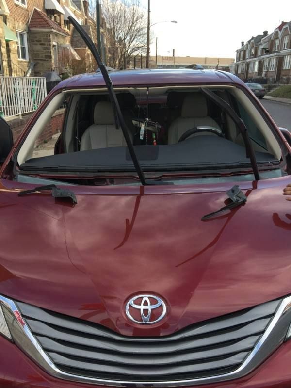 Red Toyota minivan with windshield wipers up, parked on a street in front of houses.