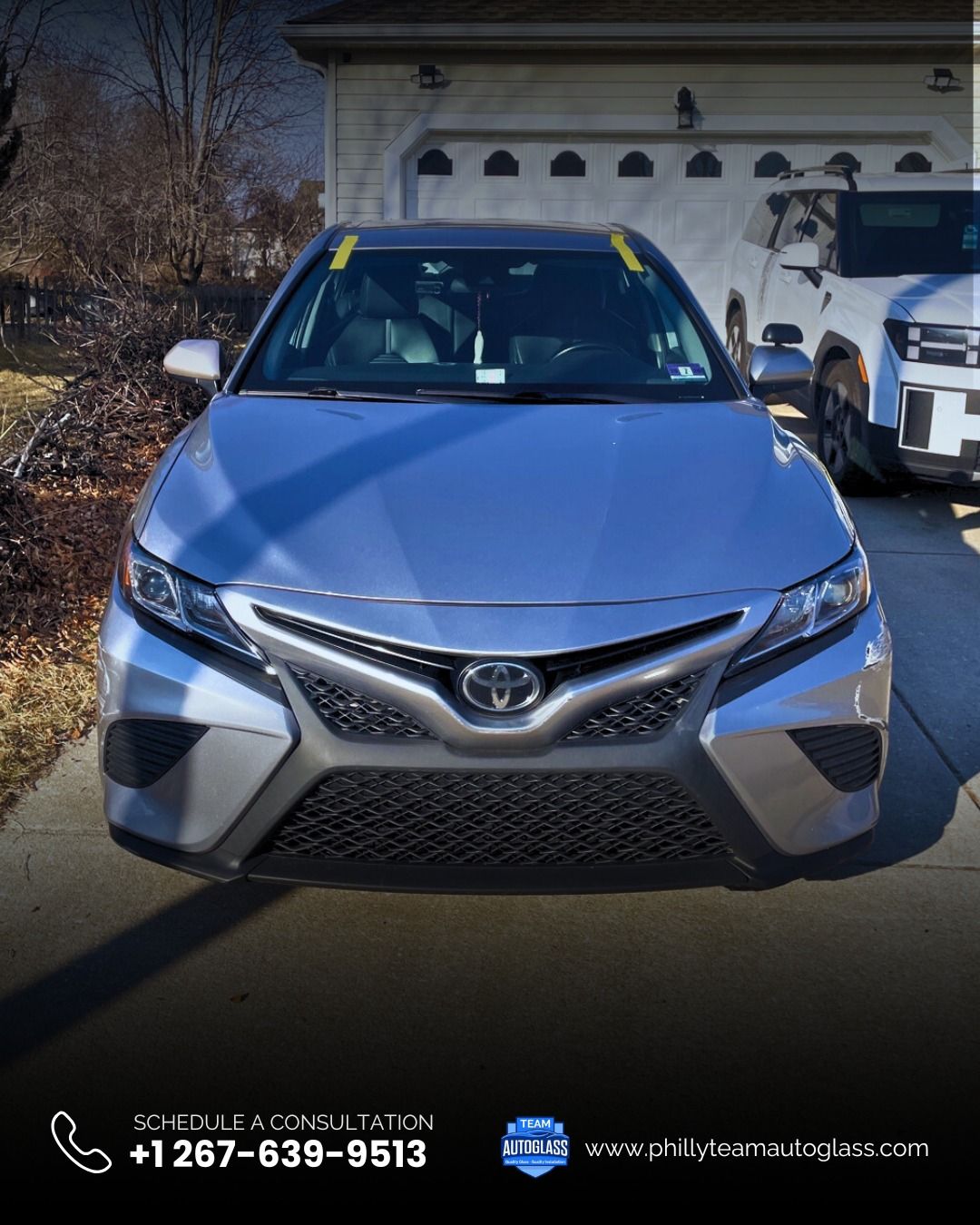 Silver Toyota Camry parked in front of a garage, with a white truck visible on the right.
