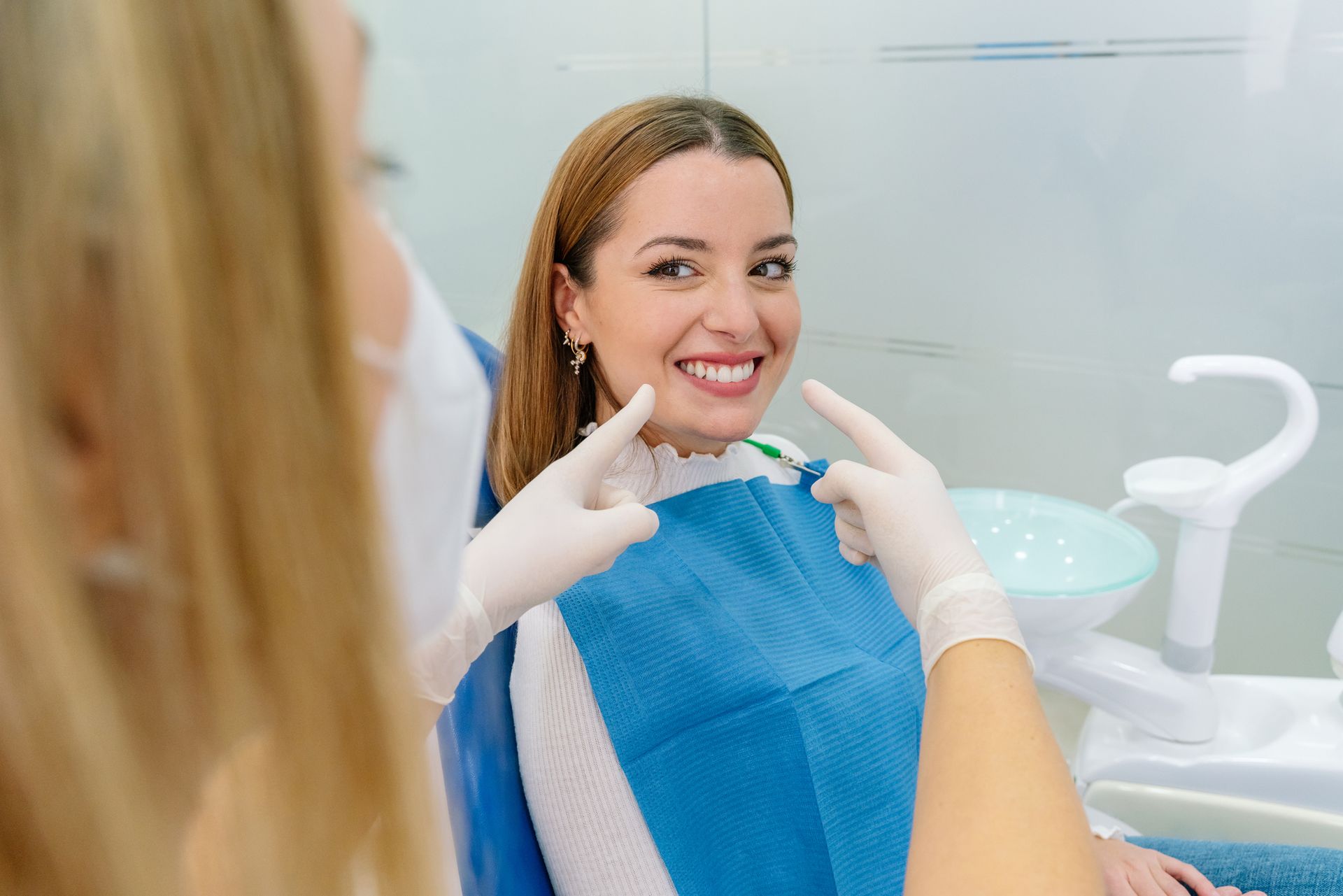 Dentist pointing at patient’s smile in bright white dental clinic.