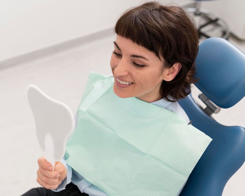 Woman in dentist chair smiles while looking at teeth in a tooth-shaped mirror.