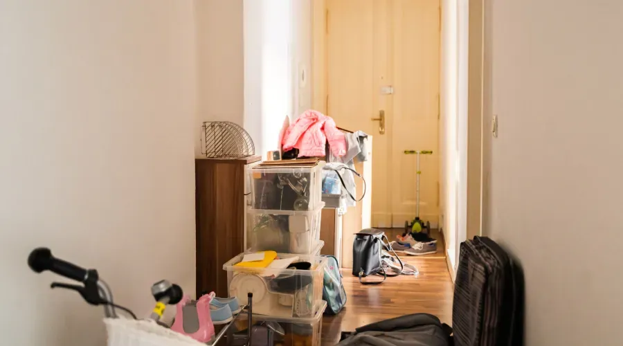 A cluttered hallway with a bicycle, boxes, and clothes near an open door and wooden floor.