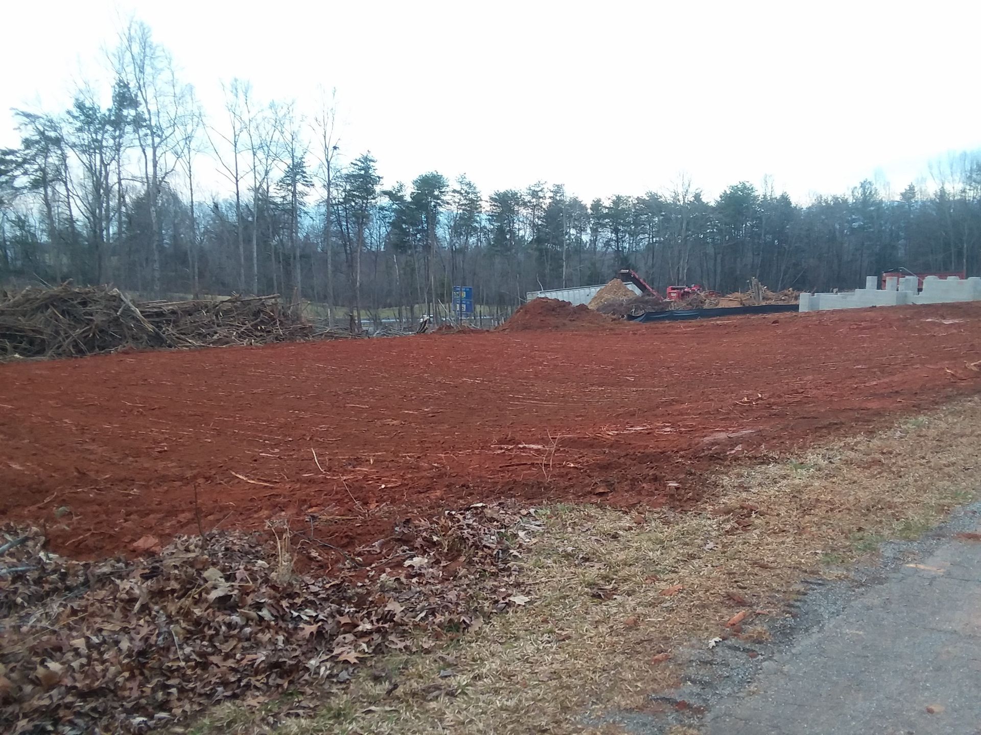 Excavators clearing land with heavy machinery on a dusty construction site near forest.
