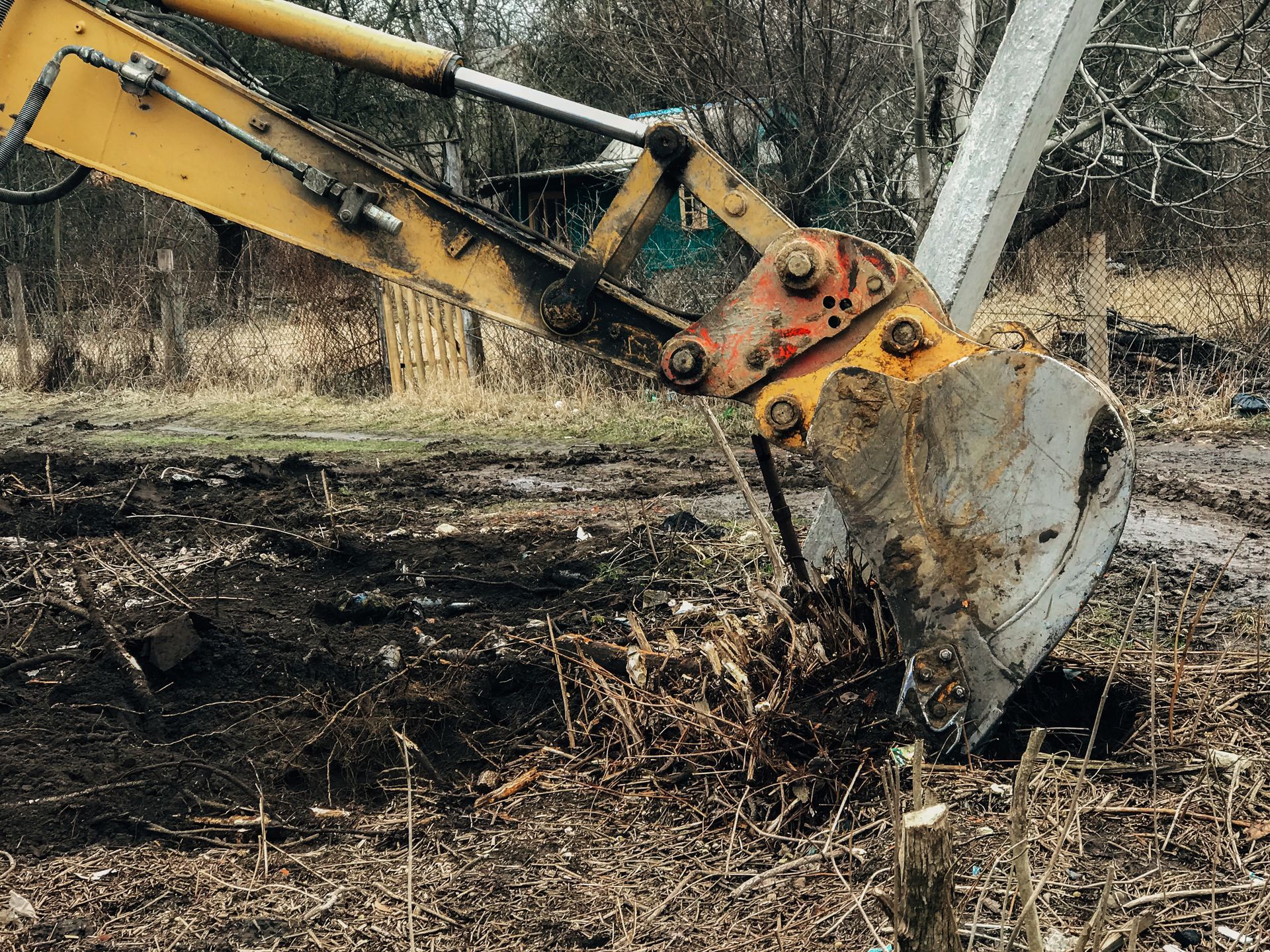 Yellow tracked excavator with a dirty bucket clearing land on a debris-strewn lot Yellow tracked excavator with a dirty bucket clearing land on a debris-strewn lot