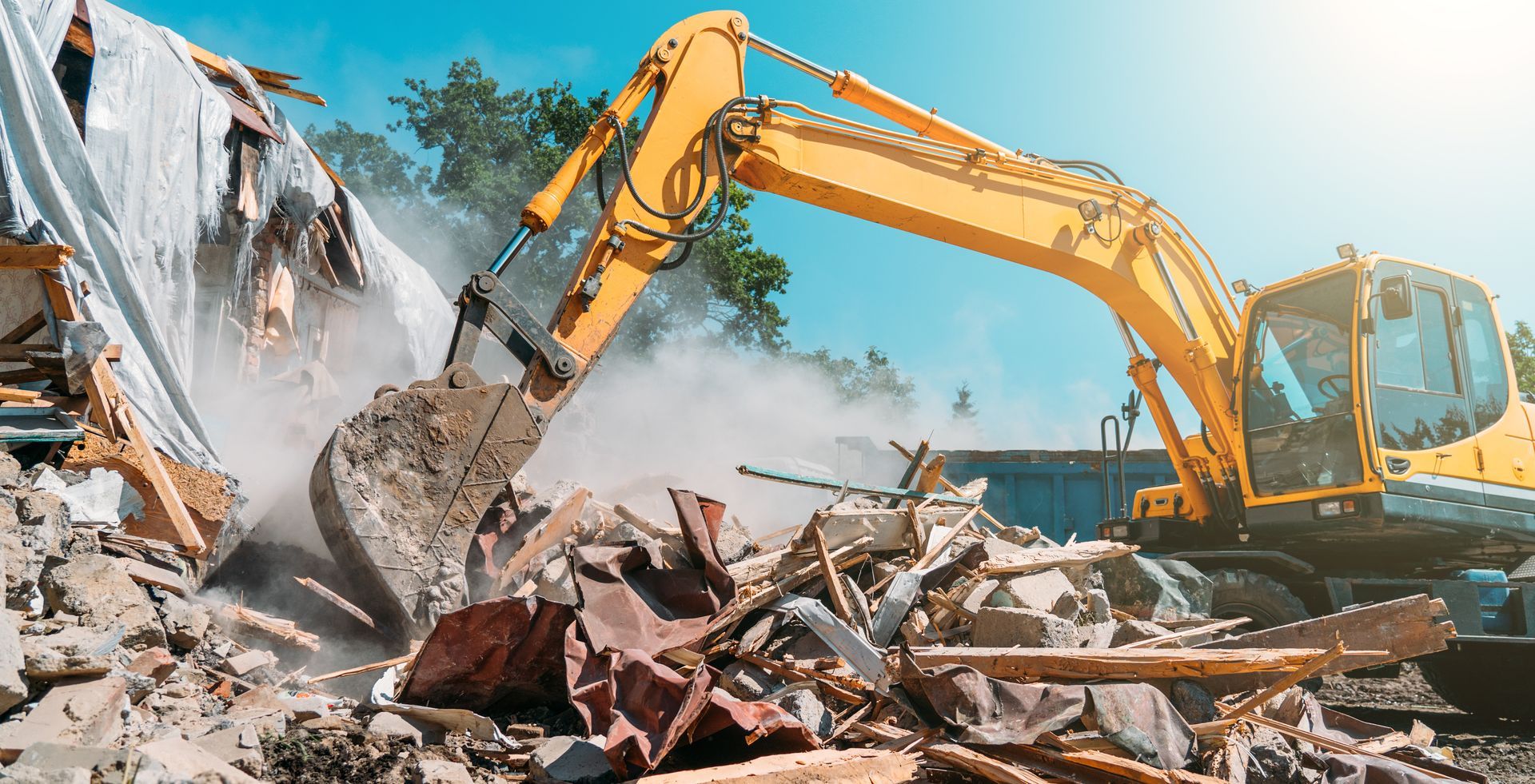 Excavator demolishing a building, lifting debris amid dust at a construction site.