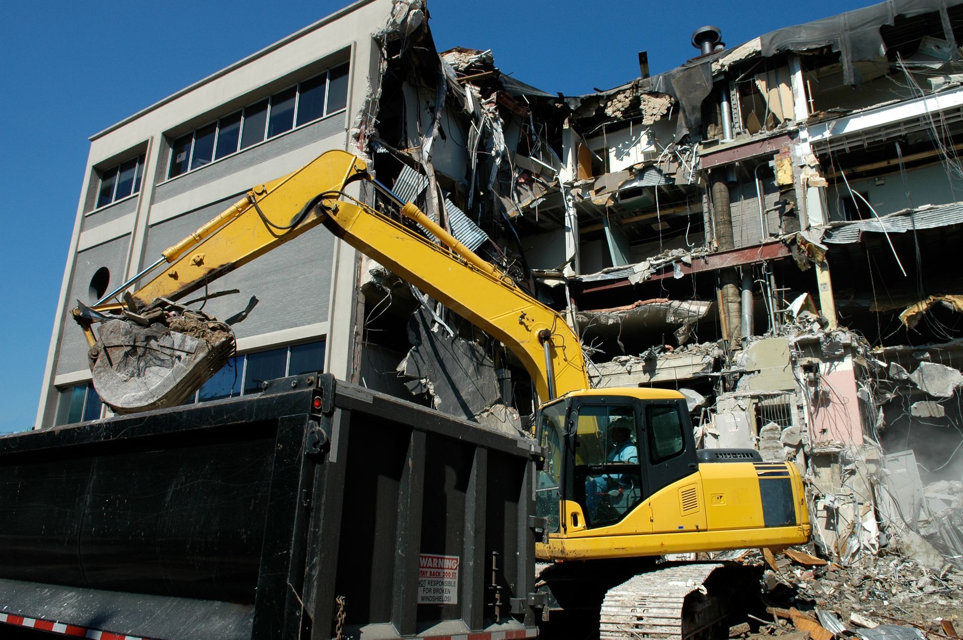 Yellow excavator operated by demolition company clearing debris from building site.