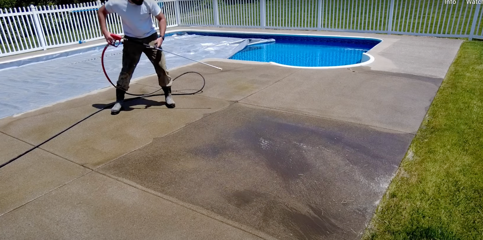 A man is cleaning a concrete patio next to a pool.