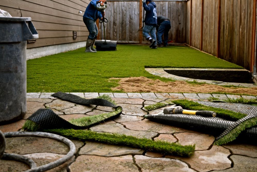 Two men are installing artificial grass in a backyard.