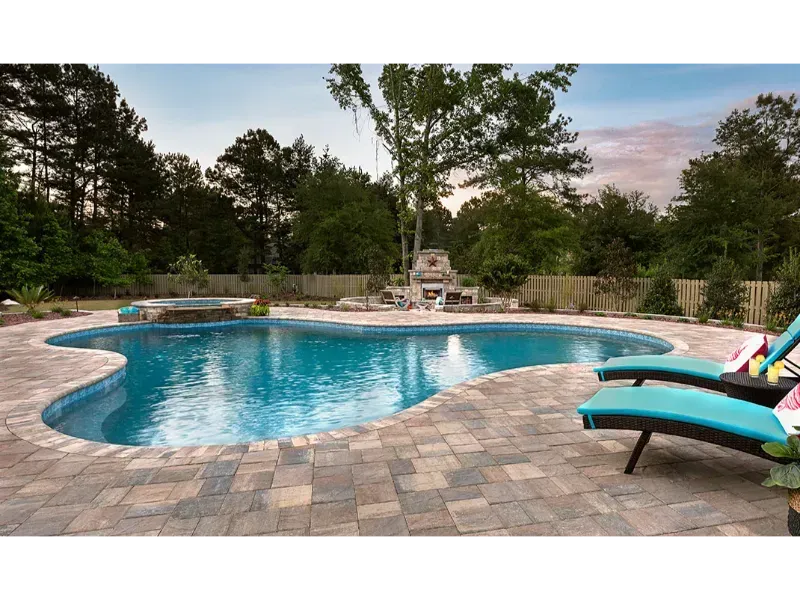 Pool with blue water and brick patio, surrounded by trees. Two lounge chairs are on the patio.