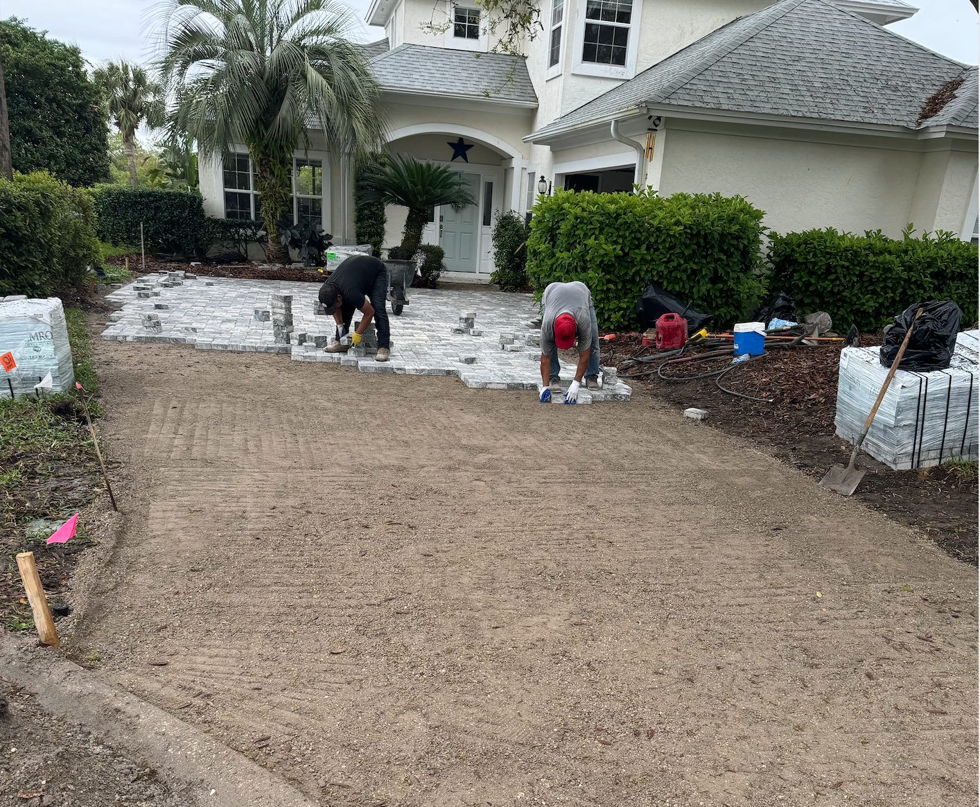 A couple of men are working on a driveway in front of a house.