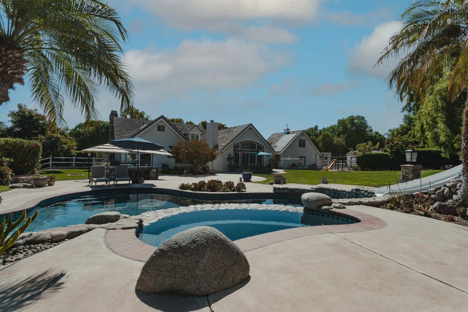 A large swimming pool is surrounded by a paver patio and chairs.