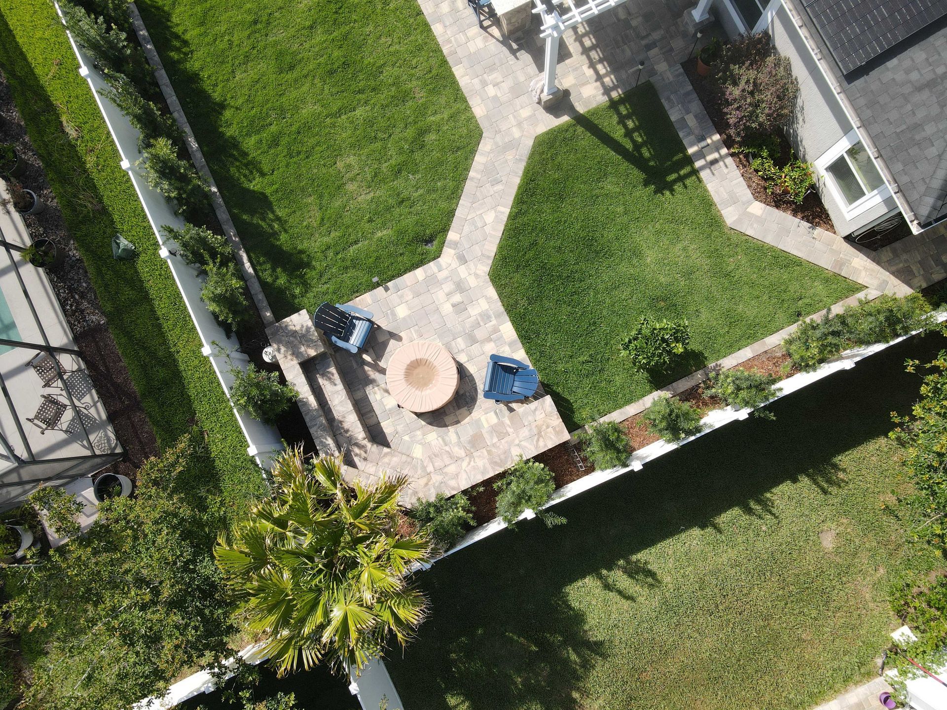 Aerial view of a backyard with a patio, fire pit, lawn, and white fence.