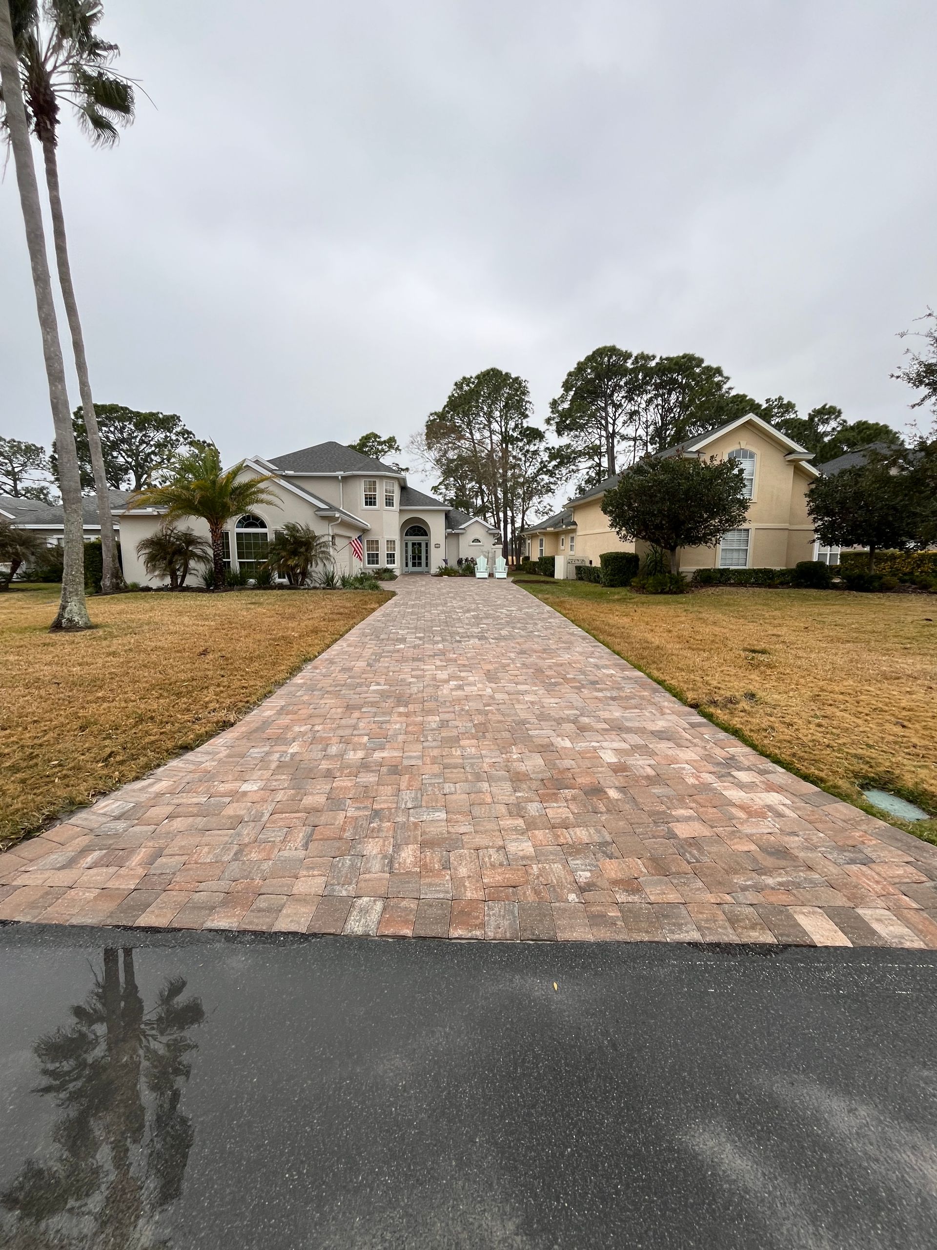 Long brick driveway leading to a large house on a cloudy day.