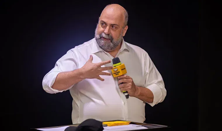 Um homem com barba está segurando um microfone e falando nele.