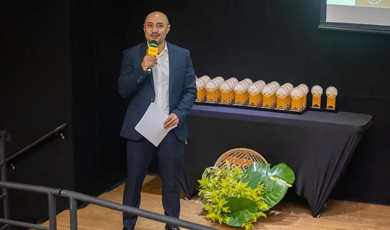 Um homem de terno está parado em frente a uma mesa segurando um microfone.