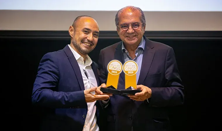 Dois homens de terno seguram troféus nas mãos.