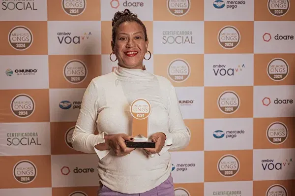 Uma mulher está segurando um troféu em frente a uma parede com logotipos nele.