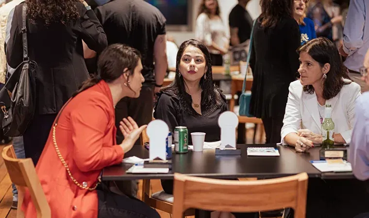 Um grupo de mulheres estão sentadas à mesa conversando entre si.