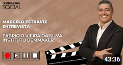 Um homem de terno sorri, ao lado de uma ripa de filme e controles de vídeo. Entrevista com Marcelo Estraviz.