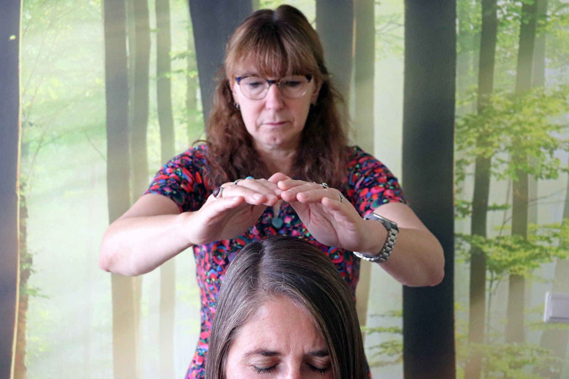 Vrouw met haar handen boven het hoofd van een andere vrouw, binnenshuis, waarschijnlijk voor energetische genezing.