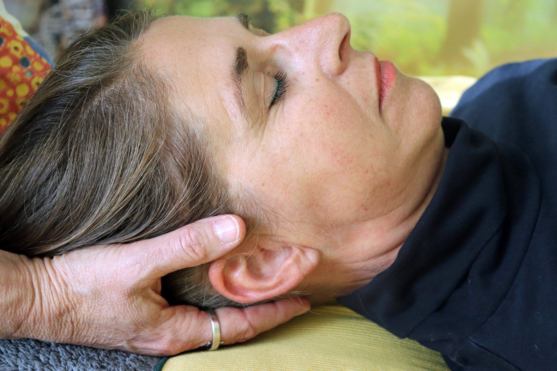 Persoon die craniosacrale therapie krijgt, hoofd in de handen, ogen gesloten, vredige uitdrukking.