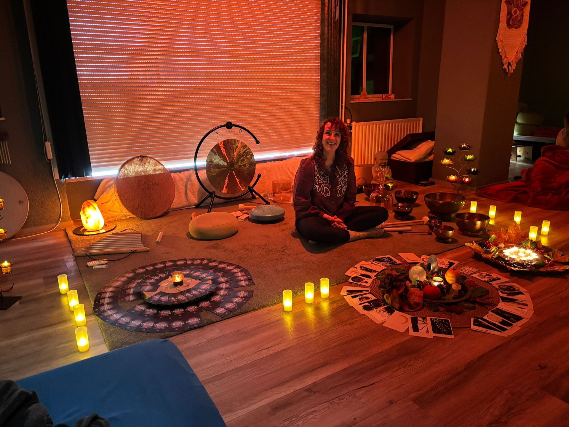Rianne zit in de yogaruimte verlicht door kaarsen, met een gong, klankschalen en decoratieve tapijten.
