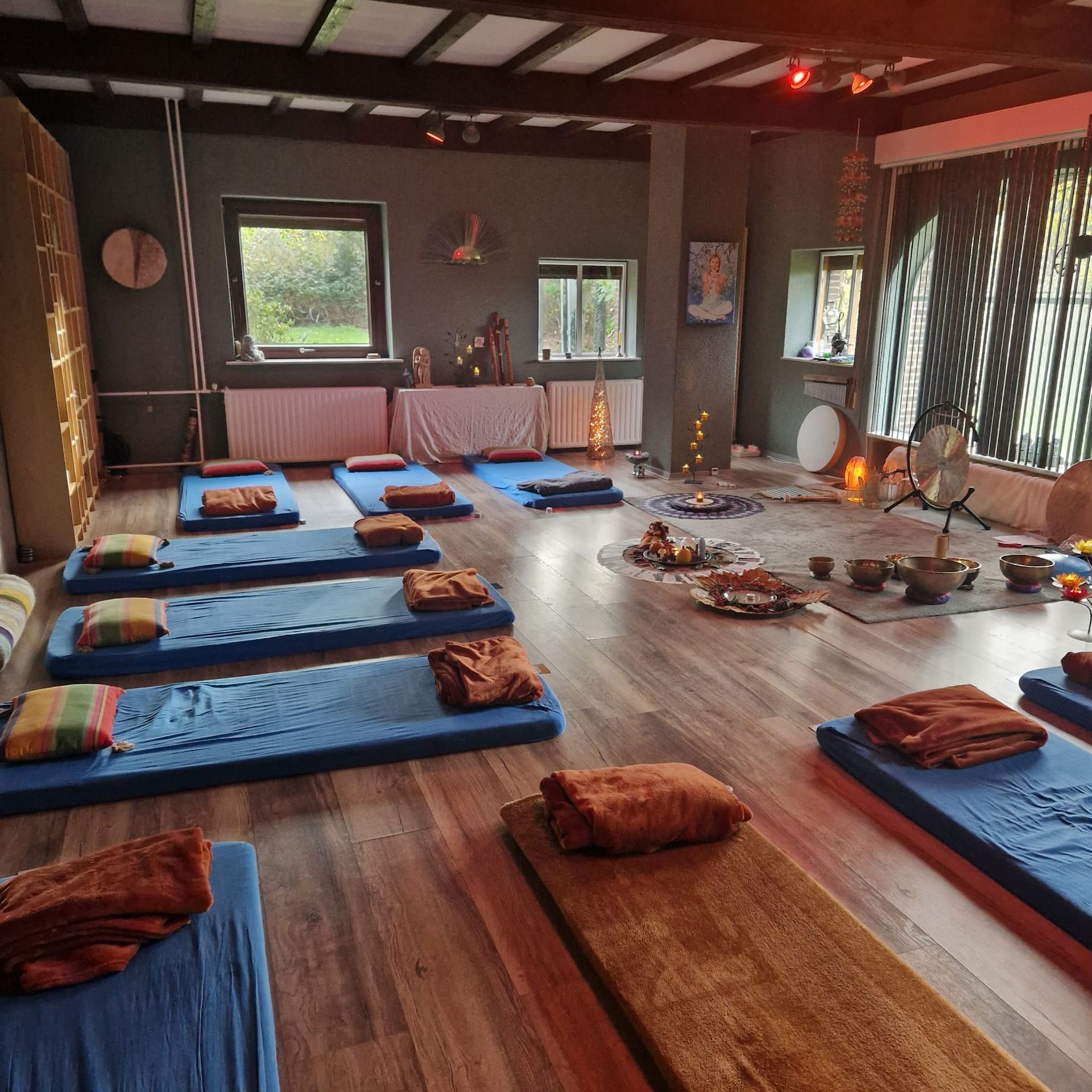 Yoga- of meditatieruimte met blauwe matten, kussens en instrumenten. Weinig licht, houten vloer en ramen.