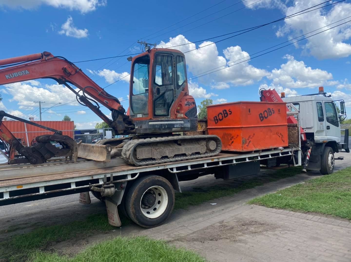 A Flatbed Truck Carrying an Excavator and an Orange Container — Bob’s Trailer Trash in Rockhampton, QLD