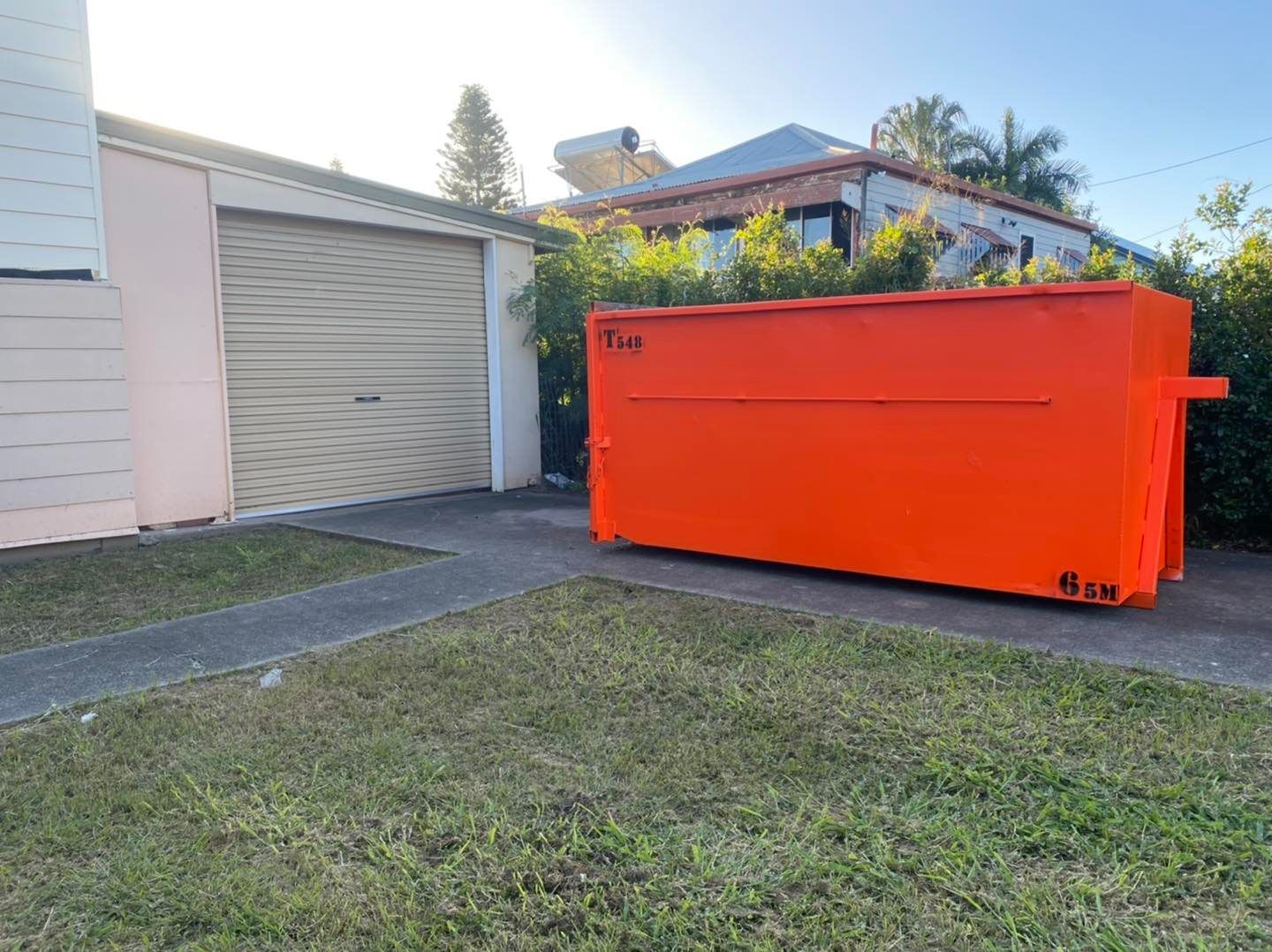Orange Dumpster on Driveway Next to Garage — Bob’s Trailer Trash in Rockhampton, QLD