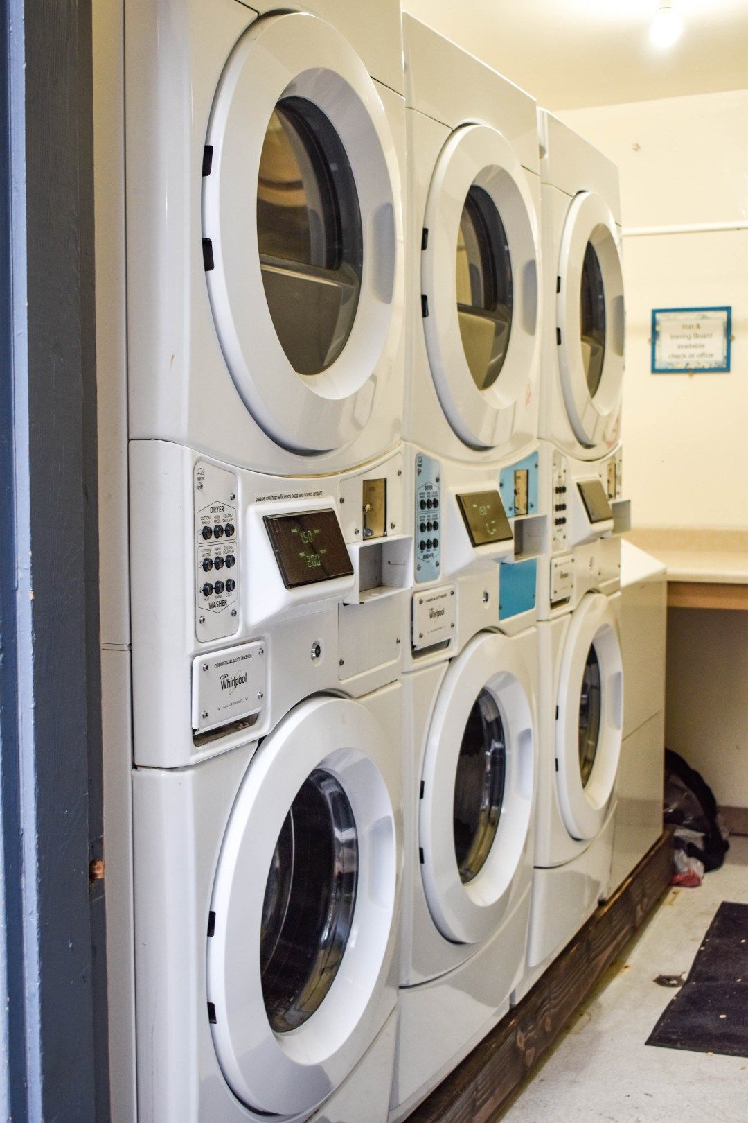 Stacked laundry machines in a laundromat, with front-loading washers and dryers along a wall.