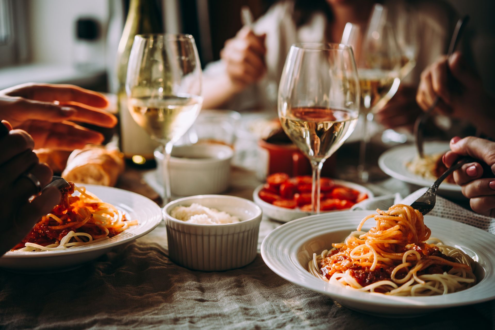 People sharing pasta and wine at a dinner table, with hands serving food and warm restaurant lighting