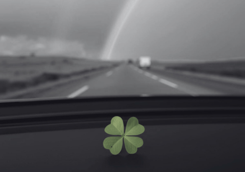 Dashboard view of a highway with a rainbow in the distance and a green clover on the dash.