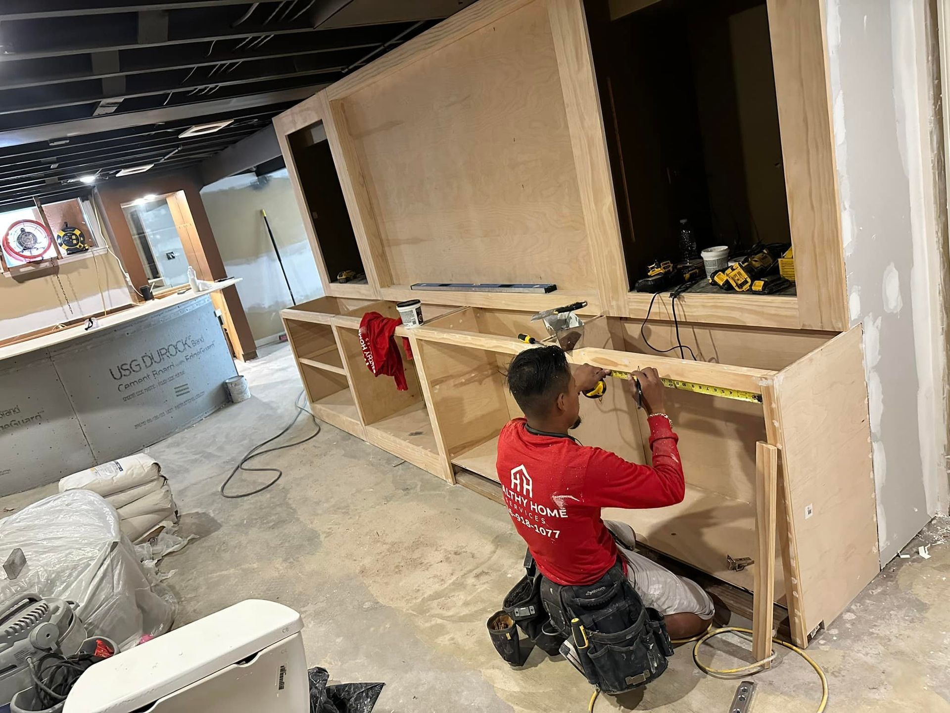 A man in a red shirt is working on a wooden cabinet.